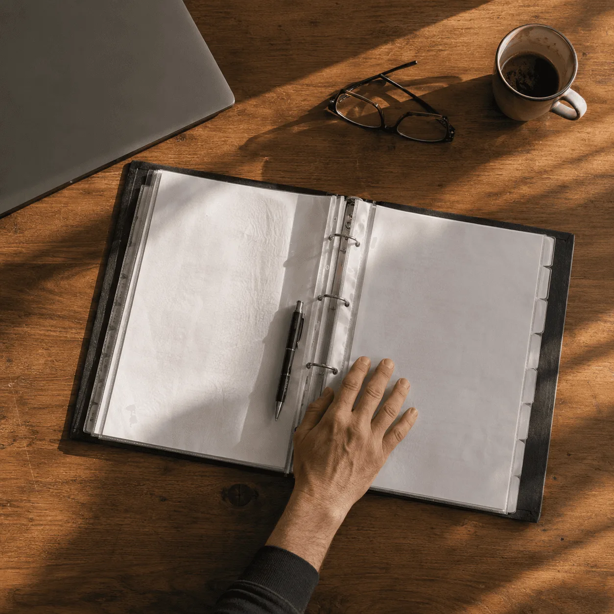 Geöffneter Ordner, Laptop und Kaffeetasse auf einem Schreibtisch.